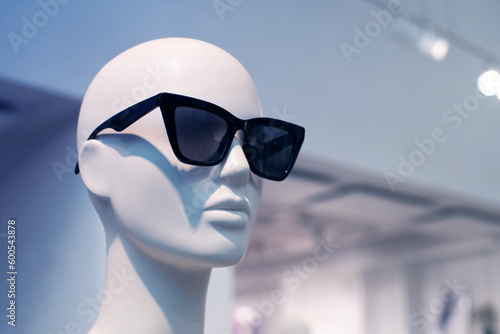 Female mannequin in black sunglasses on the showcase of a clothing store close-up, soft focus.