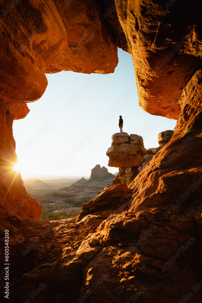 Vertical image woman standing at dramatic viewpoint of Merry-go-round Rock in Sedona Arizona admiring the golden orange sunset view.