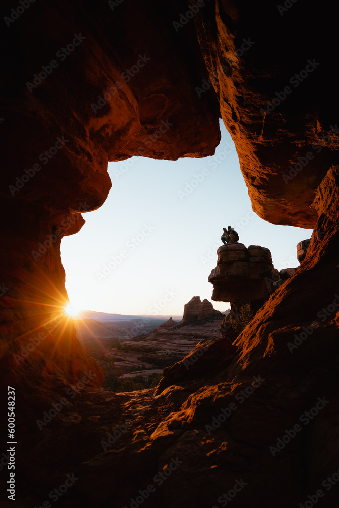 Young couple crouches at popular viewpoint rock formation in Sedona Arizona at golden orange sunset.