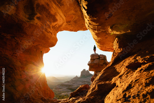 Horizontal image woman standing at dramatic viewpoint at Merry-go-round Rock in Sedona Arizona at sunset with sun flare admiring the landscape view.