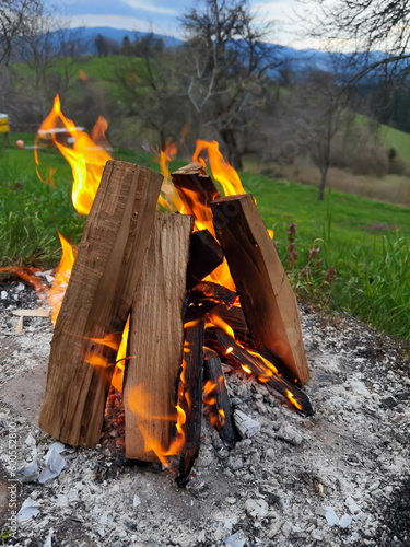 Big bonfire fire on wild nature background with stones. Close-up travel, adventure hot and bright flame light. Cozy evening in the forest outdoors. Burning wooden firewood, log, timber.