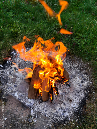 Big bonfire fire on wild nature background with stones. Close-up travel, adventure hot and bright flame light. Cozy evening in the forest outdoors. Burning wooden firewood, log, timber.