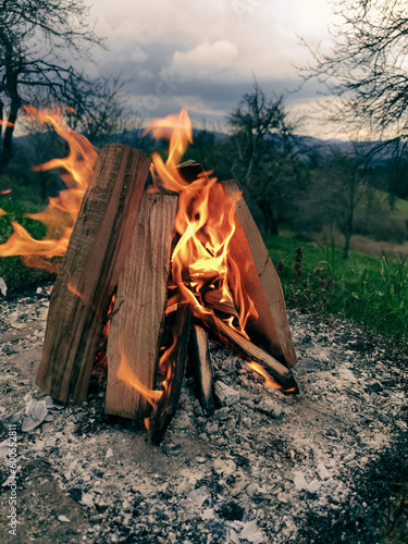 Big bonfire fire on wild nature background with stones. Close-up travel, adventure hot and bright flame light. Cozy evening in the forest outdoors. Burning wooden firewood, log, timber.