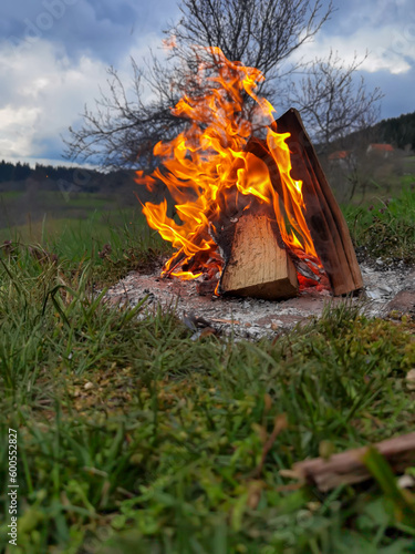 Big bonfire fire on wild nature background with stones. Close-up travel, adventure hot and bright flame light. Cozy evening in the forest outdoors. Burning wooden firewood, log, timber.