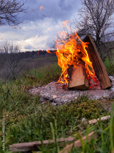 Big bonfire fire on wild nature background with stones. Close-up travel, adventure hot and bright flame light. Cozy evening in the forest outdoors. Burning wooden firewood, log, timber.