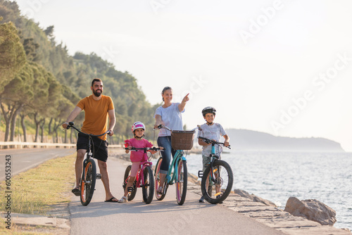 Young family, parents with two children, on bikes standing near the sea, looking at view in the direction that the mother pointing