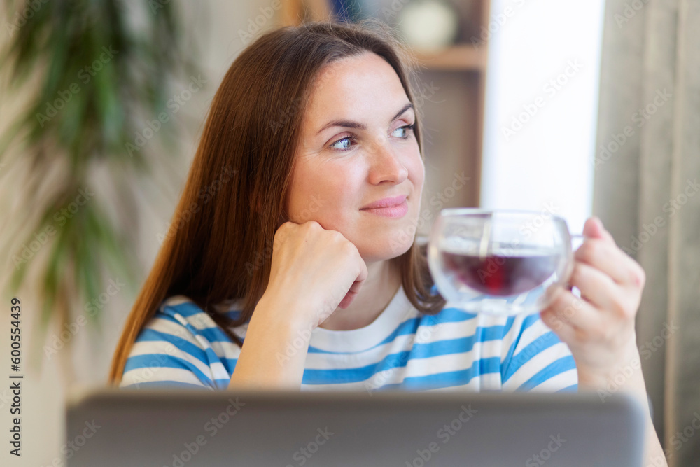 Woman taking a tea break as she sits at a table working on a laptop computer Woman taking a tea break as she sits at a table working on a laptop computer