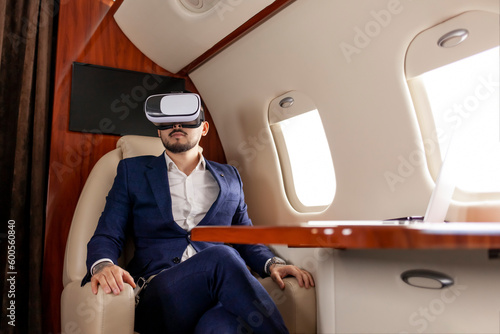 businessman in suit flies in private plane in virtual reality glasses and presses with his hands on imaginary interface