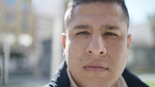 Young hispanic man standing with serious expression at street