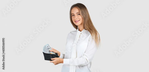 Young woman holding wallet with dollar banknotes on light background