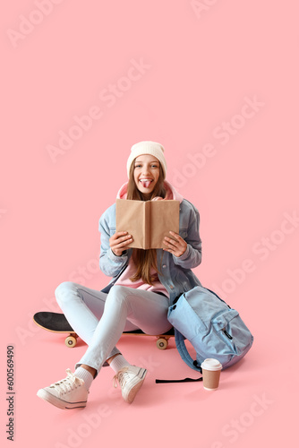 Female student with book showing tongue on pink background