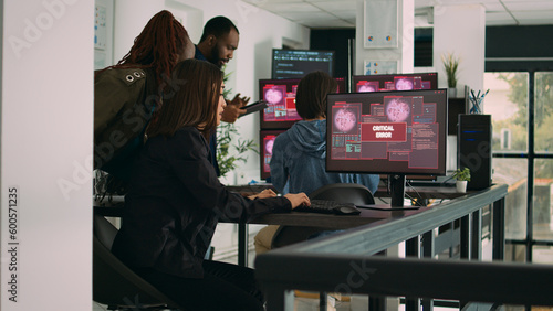 Multiethnic group of app developers reading critical errors on multiple monitors in it agency, being hacked. Working with artificial intelligence code and server database to stop program hacking.
