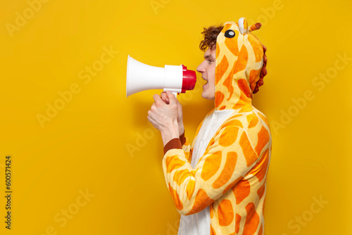 Fotografie young joyful guy in funny children's giraffe pajamas speaks into megaphone and p