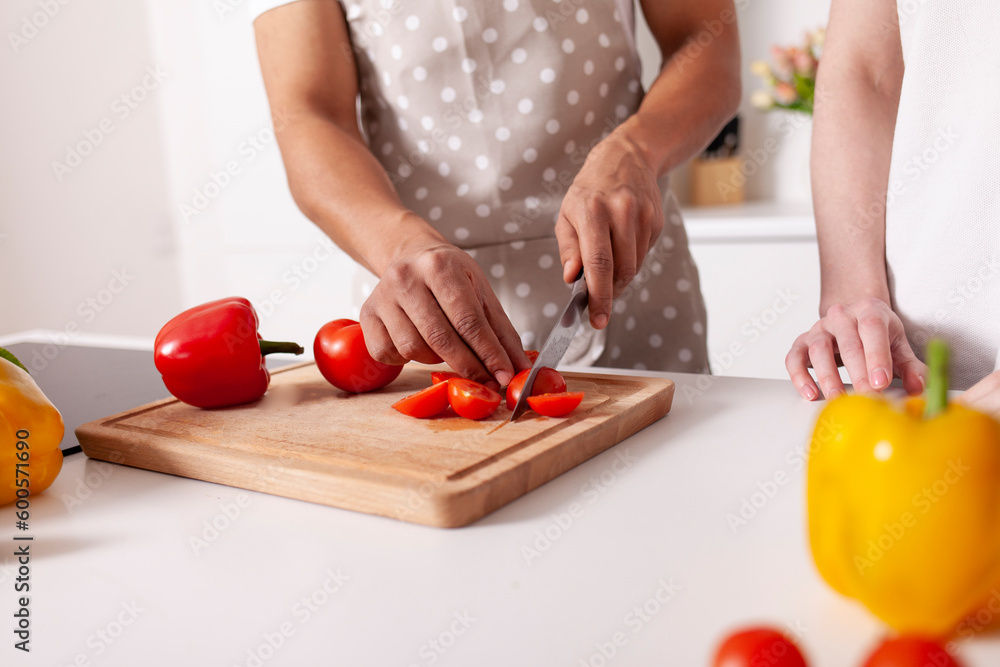 african american man in an apron cuts tomatoes in the kitchen, close-up, multiracial couple prepares african american man in an apron cuts tomatoes in the kitchen, close-up, multiracial couple prepares