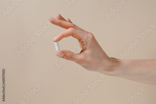 Female hand holding white pill with fingers on beige isolated background. Concept of health care, dietary supplements, treatment of depression and diseases