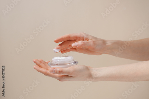 Female hand applying white moisturizing cream from glass jar on finger on beige isolated background. Beauty, skin care and aesthetics concept © Daryna 
