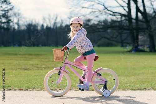 Girl riding bike in safe helmet at sunny spring park. Preschooler learning to balance on bicycle in safe helmet.