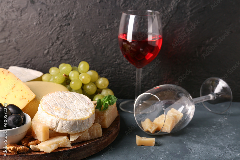 Plate with different types of tasty cheese and wine glasses on table