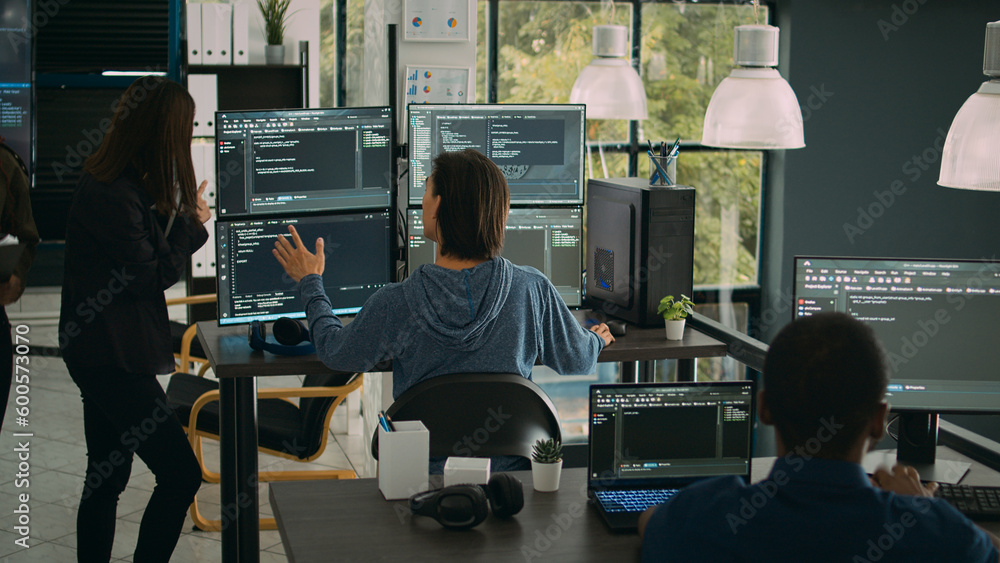 Naklejka premium System engineer checking code on multiple monitors and working with app developer colleague in it agency office. Coder analyzing algorithm on screens, developing new user interface.