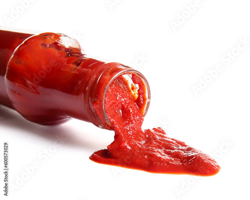 Ketchup spilled out of glass bottle on white background