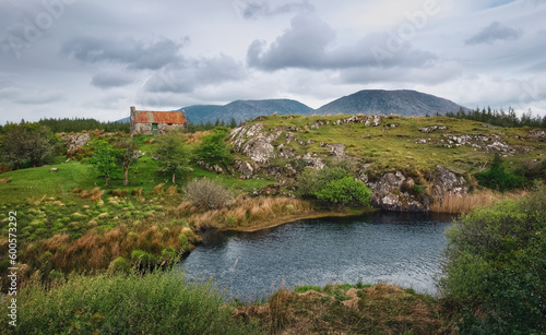 Beautiful landscape scenery with Old rusty tin roof cottage by the river with mountains in the background at Connemara National park in county Galway  Ireland 