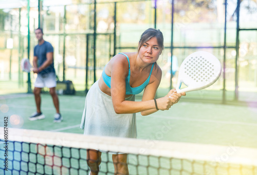 Young woman in skirt playing padel tennis on court. Racket sport training outdoors. © JackF