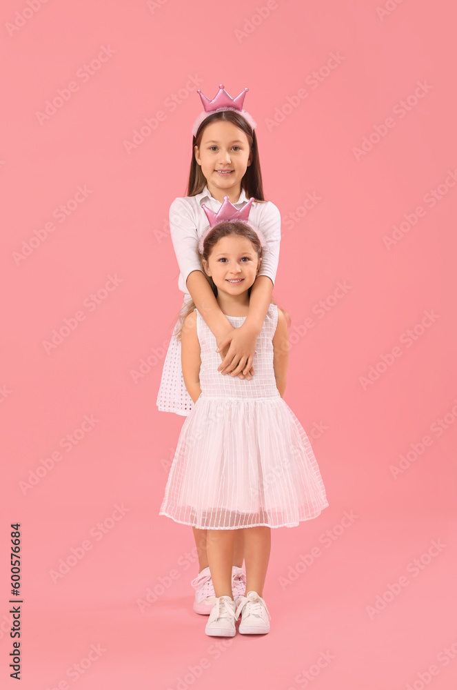 Little girls in crowns hugging on pink background. Children's Day celebration Little girls in crowns hugging on pink background. Children's Day celebration
