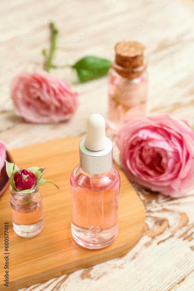 Bottles of cosmetic oil with rose extract and flowers on light wooden table Bottles of cosmetic oil with rose extract and flowers on light wooden table
