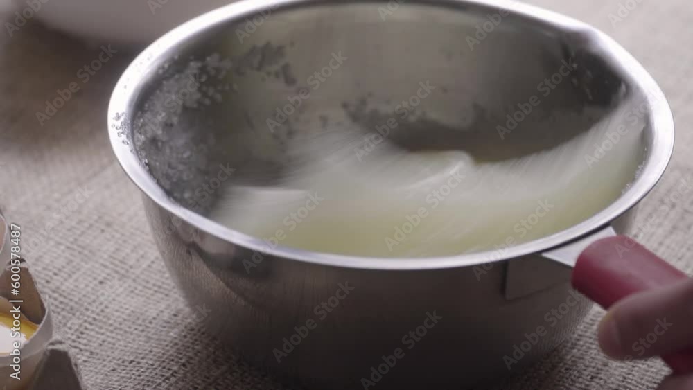 close up on hand whisk mixing sugar with egg white in steel bowl, making meringue, natural light close up on hand whisk mixing sugar with egg white in steel bowl, making meringue, natural light