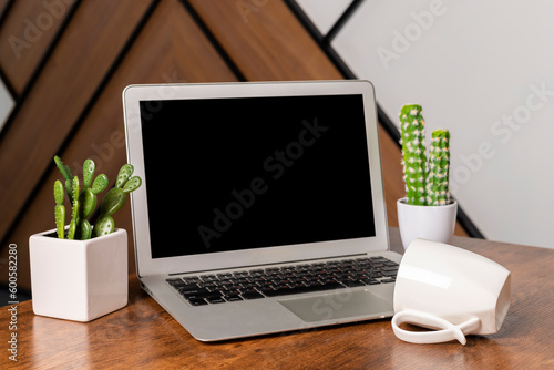 Modern Wood office desk table with laptop and blank notebook, mug and cactus plants. Home office.