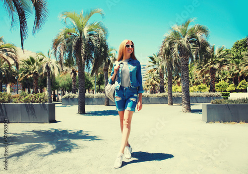 Portrait of beautiful young woman in summer park wearing backpack on palm tree background