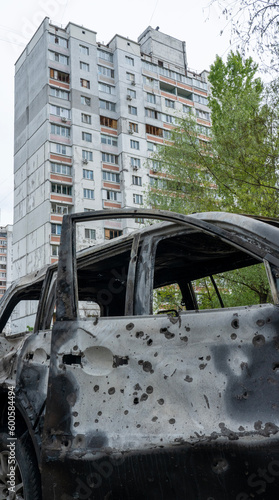 A burnt car with shrapnel holes in front of a house with broken windows after Russia's biggest missile attack on Kyiv, the concept of Russia's war against Ukraine, the genocide of the Ukrainian people photo