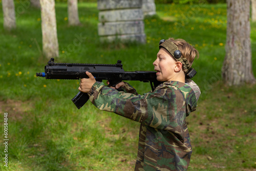 Boy weared in camouflage playing laser tag in special forest playground.