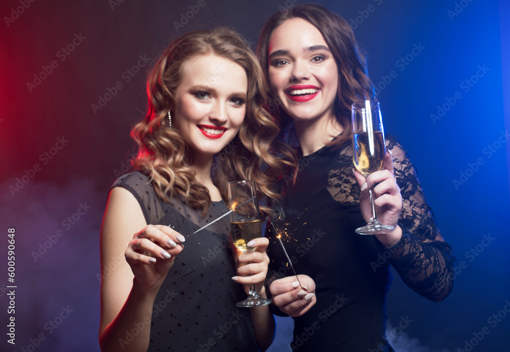 Two Young pretty women wearing black dress, holding a glass of wine and singing into microphone