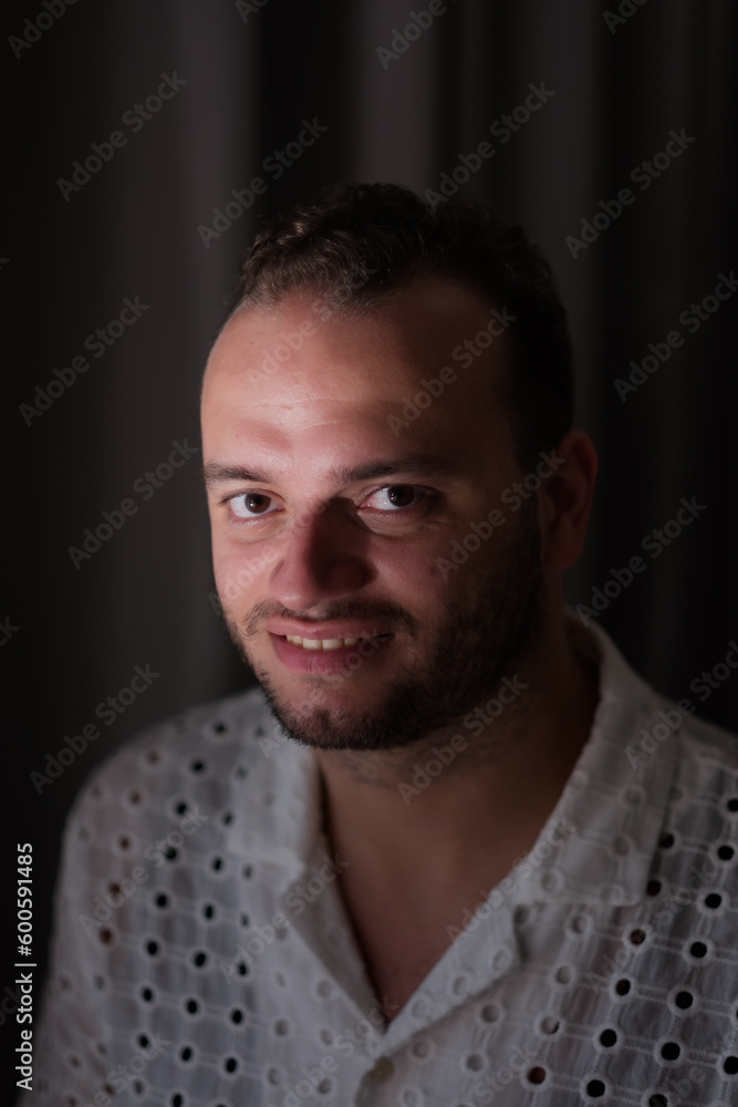 Obraz premium Posing against a dark curtain, a Middle Eastern man expresses a slight smile and handome look.