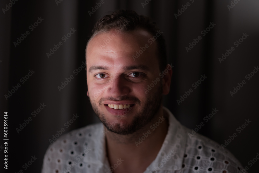 Fototapeta premium Posing against a dark curtain, a Middle Eastern man expresses a joyful smile and direct gaze at the camera.