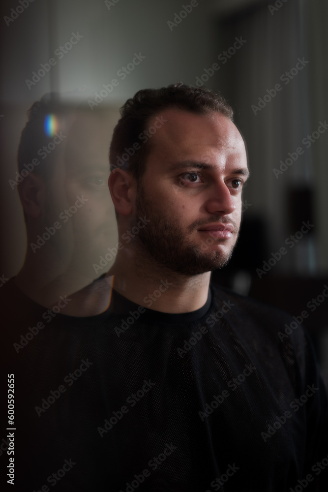 Looking at his own reflection in the mirror, a Middle Eastern man expresses a strong, confident portrait. His reflection repeats behind him off into the distance.