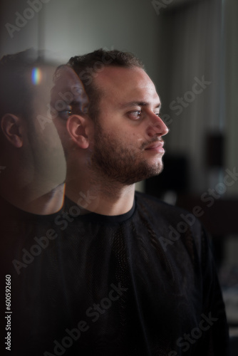 Looking at his own reflection in the mirror, a Middle Eastern man expresses a theme of contemplation and introspection, looking off into the distance with his reflection repeating behind him.