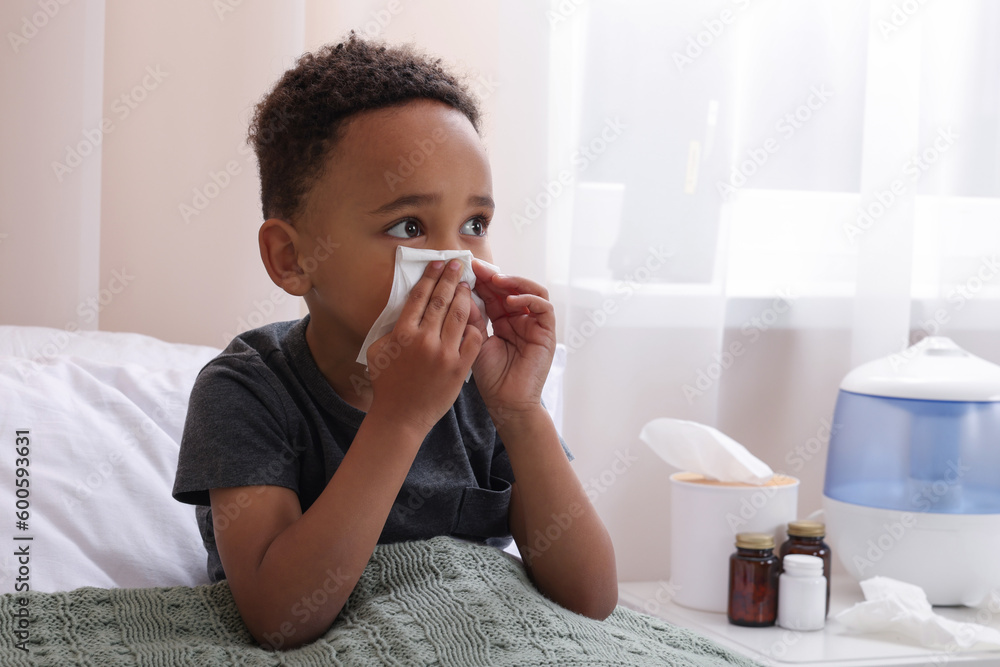 African-American boy with tissue blowing nose in bed indoors, space for text. Cold symptoms African-American boy with tissue blowing nose in bed indoors, space for text. Cold symptoms