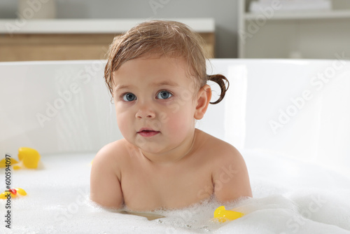 Cute little girl taking foamy bath with rubber ducks at home