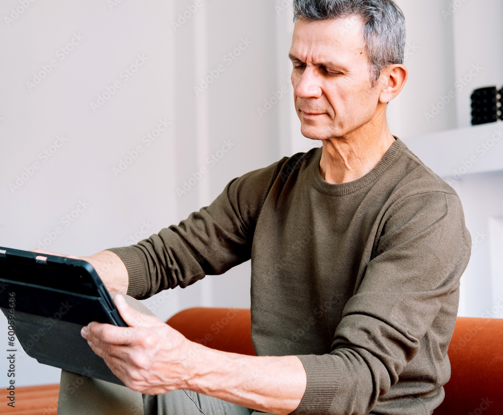 Mature caucasian man websurfing on digital tablet at home. Lifestyle, people and tehnology concept Mature caucasian man websurfing on digital tablet at home. Lifestyle, people and tehnology concept