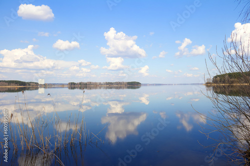 Big still lake in spring sunny day. Blue sky with beautiful cumulus clouds. Tranquil landscape.