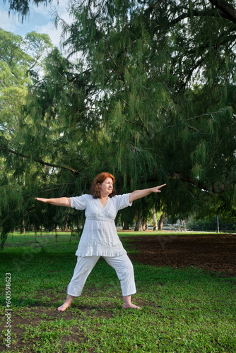 Senior Hispanic woman in white clothes practicing yoga outdoors in a park. Concepts  wellness  vitality  active and healthy lifestyle.