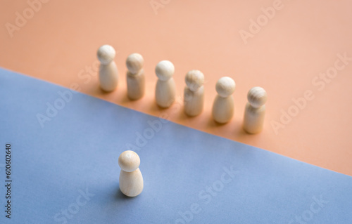 A wooden doll facing a row of dolls separated by different floor colors. Leadership concept.