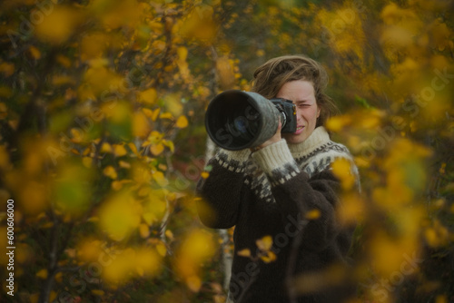 Caucasian female photographer using camera with telephoto lens in yellow autumn forest