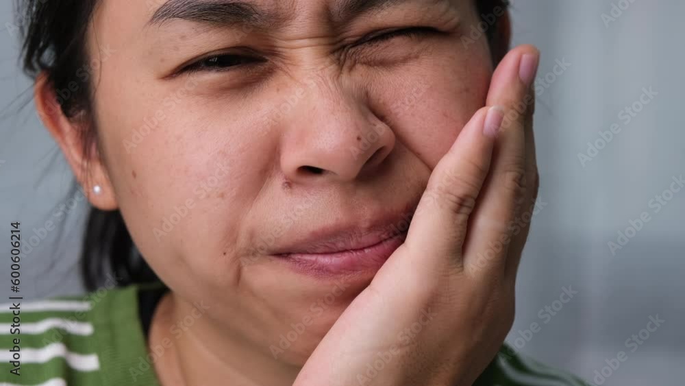Asian woman holding her hand on her cheek feeling toothache, tooth decay, gingivitis or bad breath problem. Toothache and oral health concept. Asian woman holding her hand on her cheek feeling toothache, tooth decay, gingivitis or bad breath problem. Toothache and oral health concept.