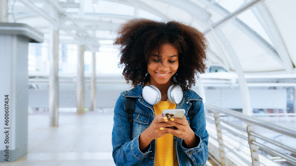 Happy young afro woman listening to playlist music with wireless headphones while wearing yellow shirt and jeans jacket outdoor - obrazy, fototapety, plakaty 
