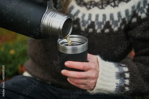 Woman pouring a tea from thermos outdoors