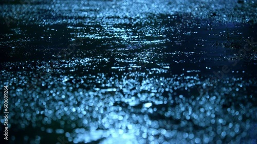 Closeup of rain drops falling on puddle with lights reflection on city sidewalk, Rain drop with street lights at night, Weather or environment