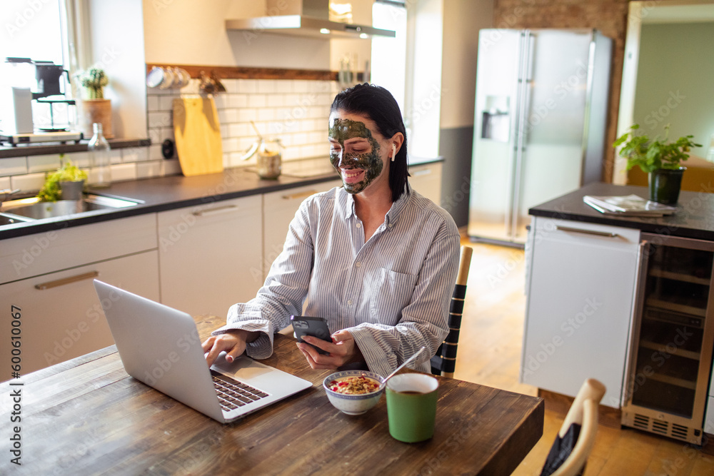 Young adult woman using her phone and laptop while having breakfast in the morning Young adult woman using her phone and laptop while having breakfast in the morning